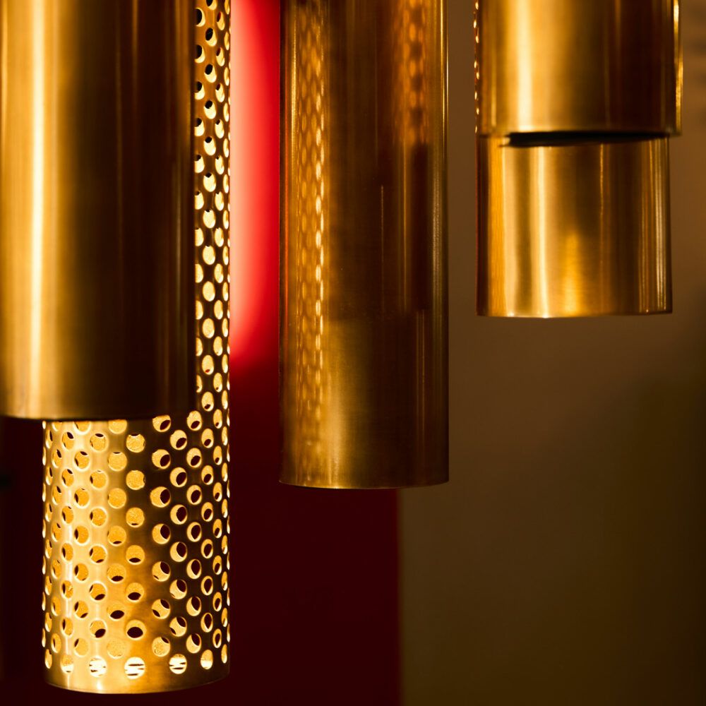 Perforated and patinated brass pendant light: Layered lighting and bespoke compositions