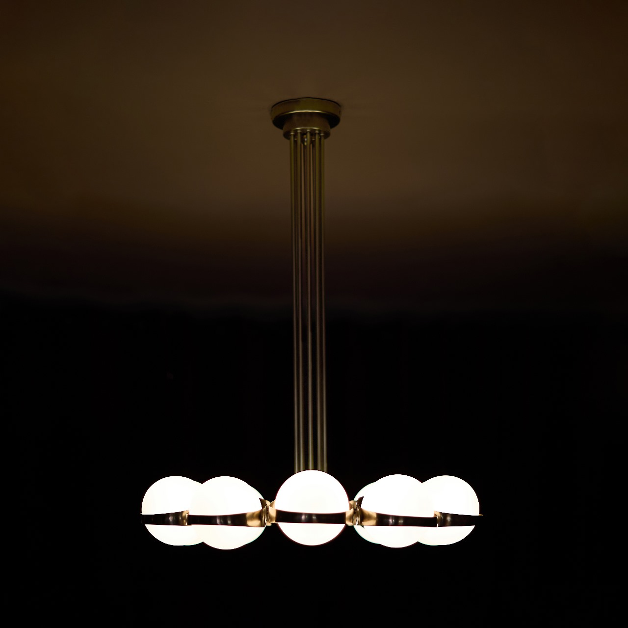 Art Deco brass chandelier featuring a circular structure and a central stem composed of vertical lines. Blown glass opal shades, soft light, and aged brass finish.